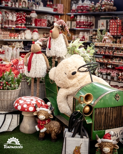 Grand ours en peluche beige installé dans une voiture décorative verte, entouré de rennes et d'un champignon rouge en